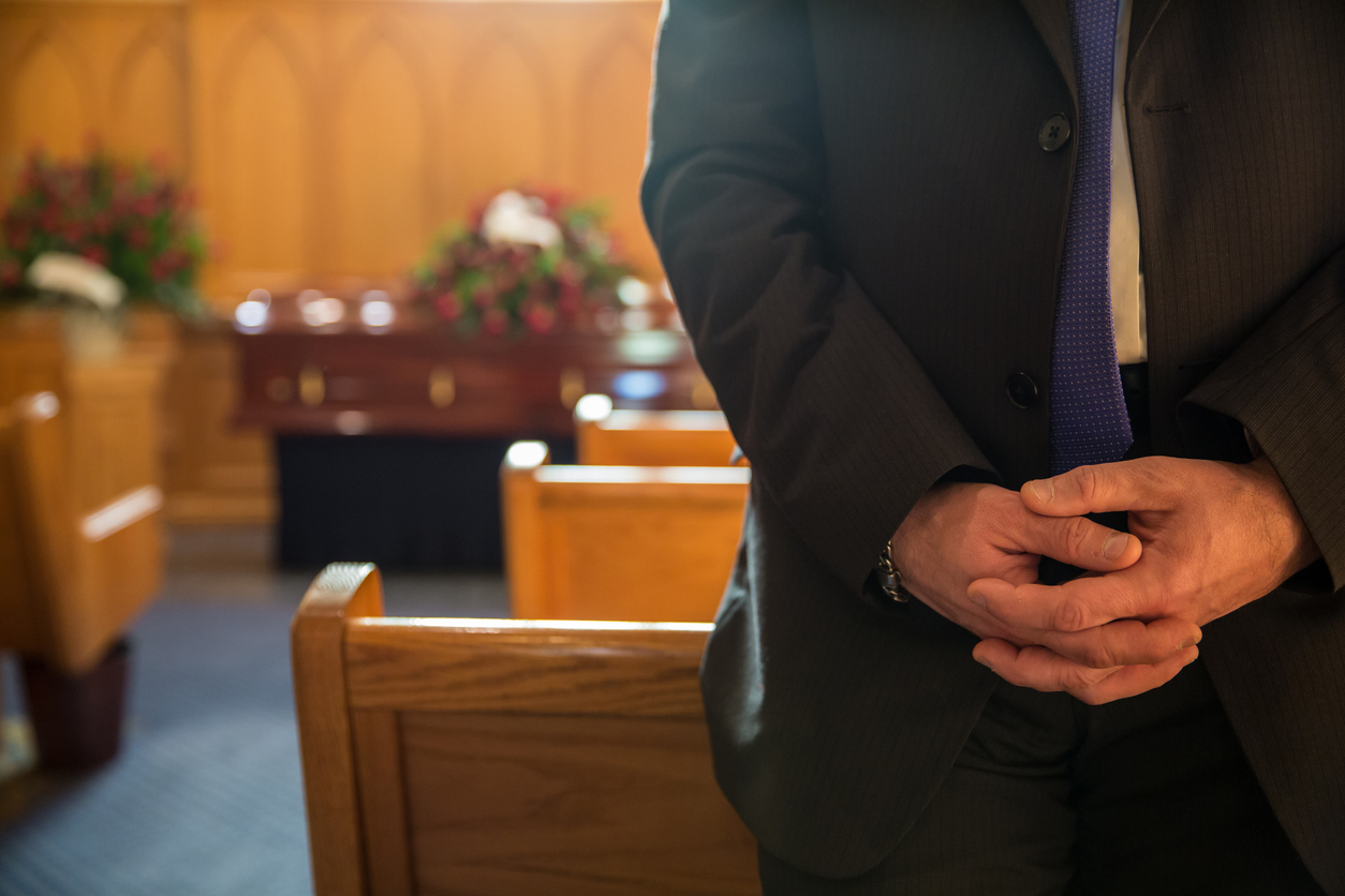 Man stands wearing a suit with his hands clasped inside a chapel before a funeral service